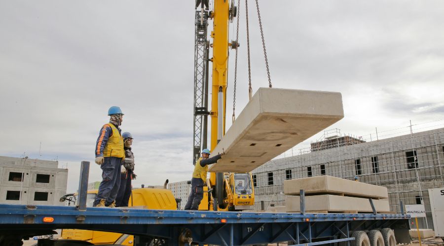 Procedury komunikacji między operatorem żurawia a sygnalistą Bezpieczna i skuteczna praca żurawia budowlanego wymaga ścisłej współpracy między operatorem a sygnalistą. Prawidłowa komunikacja między tymi osobami minimalizuje ryzyko wypadków, zapewnia płynność działań i umożliwia sprawną realizację zadań transportowych. W niniejszym artykule omówiono procedury, standardy oraz techniki komunikacji operator–sygnalista w różnych warunkach pracy. Komunikacja operator–sygnalista – niezbędne wsparcie przy obsłudze żurawia budowlanego W przypadku żurawi szynowych, wieżowych czy samojezdnych, sygnalista stanowi kluczowe ogniwo w procesie podnoszenia i przemieszczania ładunków. Sygnały dla operatora żurawia są przekazywane w sposób jednoznaczny, aby uniknąć błędów. Sygnalista do obsługi żurawia nadzoruje porozumiewanie się podczas transportu pionowego i odpowiada za koordynację pracy dźwigu z innymi ekipami na placu budowy. Jakie są obowiązki sygnalisty podczas pracy z operatorem żurawia? Jest to: Nadzór nad bezpiecznym ruchem ładunku – kontrola strefy podnoszenia i opuszczania. Przekazywanie jasnych i zgodnych ze standardem sygnałów – eliminowanie niejednoznacznych gestów. Monitorowanie otoczenia – identyfikowanie potencjalnych zagrożeń w strefie pracy. Utrzymywanie ciągłej łączności z operatorem – zapewnienie reakcji w czasie rzeczywistym. Procedury i zasady współpracy operator – sygnalista na budowie Prawidłowa komunikacja podczas przenoszenia ładunków to fundament bezpieczeństwa. Wykorzystuje się bezpieczne systemy porozumiewania się przy dźwigowych pracach, oparte o określone procedury BHP przy podnoszeniu ładunków oraz kody porozumiewawcze przy dźwignicy. Każdy element procedur komunikacji na budowie musi być realizowany zgodnie z przepisami i instrukcjami producenta sprzętu, aby zapewnić bezpieczeństwo pracy żurawia. Kiedy operator żurawia może odmówić wykonania polecenia sygnalisty? Gdy polecenie jest sprzeczne z zasadami BHP, zagraża bezpieczeństwu ludzi, konstrukcji lub sprzętu. Jakie są konsekwencje nieprawidłowej komunikacji między operatorem żurawia a sygnalistą? Są to przede wszystkim wypadki z udziałem ludzi lub sprzętu, opóźnienia w harmonogramie prac i szkody materialne. Jakie są procedury bezpieczeństwa w komunikacji z operatorem żurawia? Obowiązuje: Stosowanie uzgodnionego zestawu sygnałów – zapobiega pomyłkom. Utrzymanie widoczności sygnalisty dla operatora – gwarantuje poprawny odbiór poleceń. W przypadku utraty kontaktu – natychmiastowe wstrzymanie pracy. Regularne szkolenia przypominające – aktualizacja wiedzy zgodnie z przepisami. Sygnalizacja przy pracach dźwigowych – sposoby działania W praktyce stosuje się dwie główne metody: wizualną (gesty, tablice, wskaźniki) oraz radiową (łączność głosowa). Dobór zależy od warunków terenowych, widoczności i rodzaju zadania. Niezależnie od formy, należy przestrzegać standardów komunikacji operatorskiej, które gwarantują jednolitość sygnałów i minimalizują ryzyko nieporozumień. Standardy sygnalizacji wizualnej dla podnośników Komunikacja wizualna na placu budowy opiera się na jednoznacznych sygnałach gestowych na budowie, które przekazuje sygnalista żurawia. W sytuacjach awaryjnych stosuje się specjalne znaki umowne operatorów dźwigu. W jakiej odległości powinien znajdować się sygnalista od ładunku? Zwykle w odległości zapewniającej pełną widoczność zarówno ładunku, jak i operatora, najczęściej 2–5 metrów, poza strefą zagrożenia. Jak sygnalizować sytuacje awaryjne operatorowi żurawia? Poprzez ustalony sygnał zatrzymania – zazwyczaj wyraźny ruch ręki w górę i w bok lub natychmiastowy komunikat radiowy. Czy istnieją międzynarodowe standardy komunikacji dla operatorów żurawi? Tak, m.in. ISO 16715 określające jednolite gesty i procedury. Jak należy komunikować kierunek i prędkość ruchu ładunku? Kierunek gestem wskazującym ruch, prędkość – tempem i rozmiarem gestu. Gesty sygnalizacyjne dla operatorów dźwignic Jakie są podstawowe znaki używane w komunikacji między operatorem żurawia a sygnalistą? Główne gesty sygnalisty żurawia, to: Podnieś ładunek – ręka uniesiona, ruch okrężny w górę. Opuść ładunek – ręka opuszczona, ruch okrężny w dół. Stop – ręka wyciągnięta do przodu, dłoń otwarta. Przesuń w bok – ręka wskazuje kierunek. Zmniejsz prędkość – powolny, mały gest w danym kierunku. Komunikacja radiowa przy obsłudze sprzętu budowlanego System sygnalizacji budowlanej często obejmuje komunikację radiową operator–sygnalista jako wsparcie dla sygnałów wizualnych. Procedura obejmuje potwierdzenie gotowości, wydawanie krótkich, jednoznacznych komend, potwierdzenia odbioru i zakończenia manewru. Stosuje się wyłącznie kanały radiowe dedykowane do pracy na budowie, aby uniknąć zakłóceń. Jak wygląda procedura komunikacji radiowej między operatorem żurawia a sygnalistą? Jest to: Nawiązanie łączności i identyfikacja rozmówców. Przekazanie komendy w ustalonej formie. Potwierdzenie odbioru i powtórzenie polecenia. Wykonanie manewru i zgłoszenie jego zakończenia. Szkolenie sygnalistów do prac transportowych na budowie Szkolenie sygnalistów dźwigowych obejmuje teorię, praktykę oraz elementy certyfikacji sygnalistów. Program koncentruje się na technikach sygnalizacji, przepisach BHP, procedurach awaryjnych i współpracy z operatorem. Czy sygnalista musi posiadać specjalne uprawnienia? W Polsce wymagane jest przeszkolenie i potwierdzenie kwalifikacji zgodnie z przepisami BHP, choć nie zawsze formalne uprawnienia UDT. Jakie szkolenia powinien przejść sygnalista? Szkolenie teoretyczne z przepisów i standardów, praktyczne z obsługi sygnałów, oraz z procedur awaryjnych.